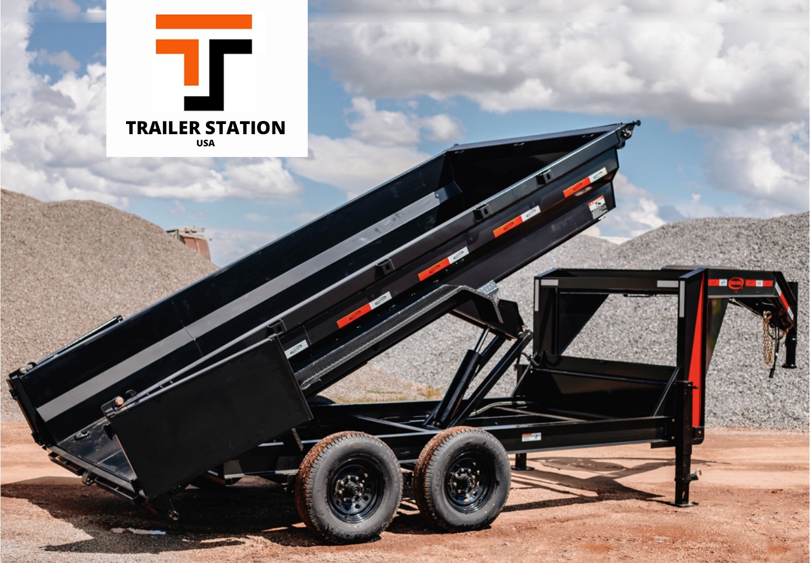 A large black dump trailer with gravel piles in the background